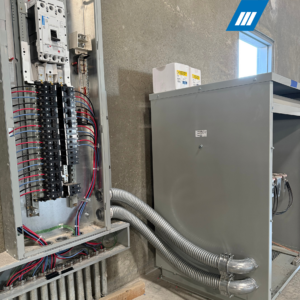 Electrical panel with multiple circuit breakers, neatly arranged wiring, red and black wires connected to terminals, and a large electrical enclosure with conduits attached.